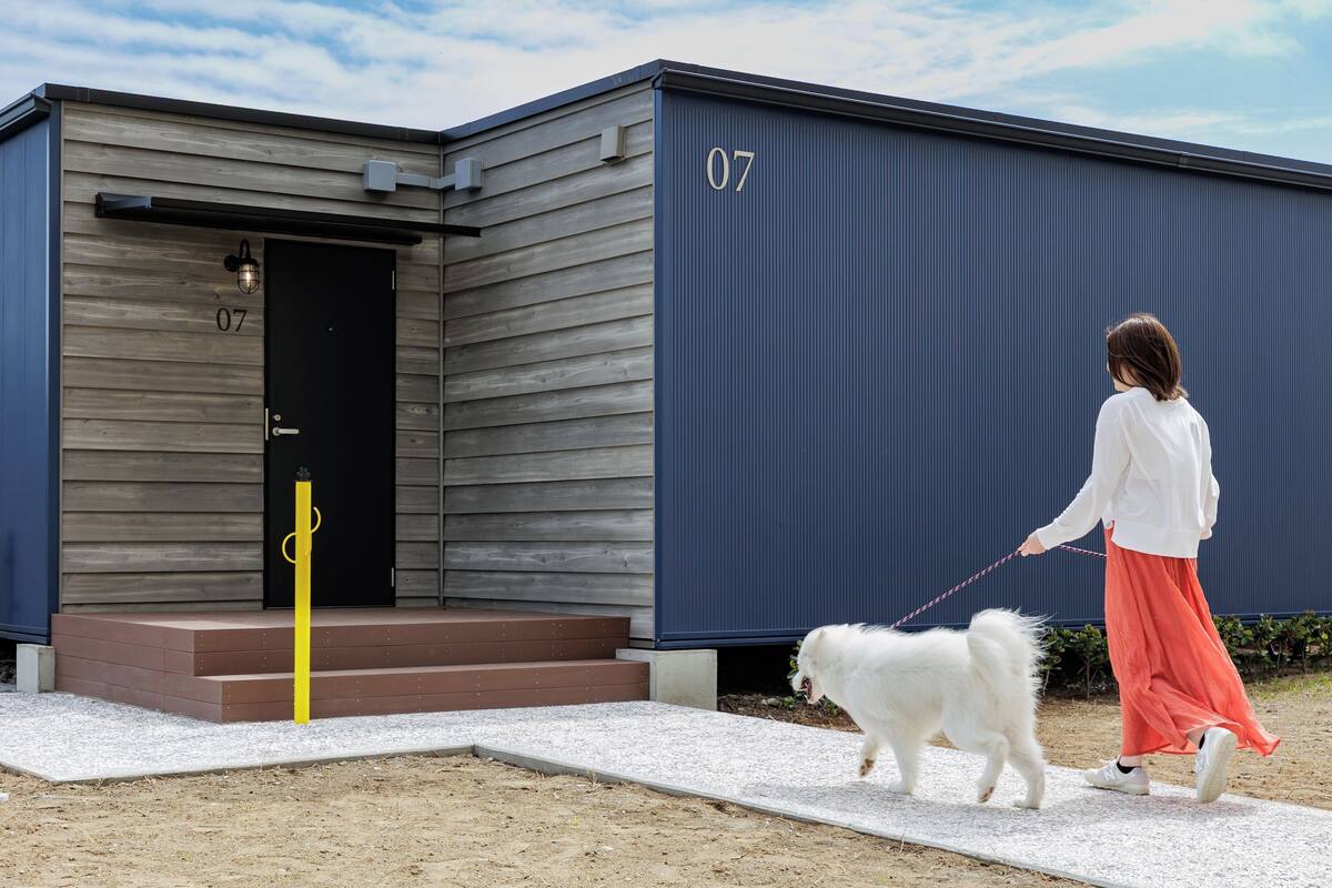 A person walking a white dog on a leash in front of a building with the number 07 on the door and a small set of steps leading up to the entrance.