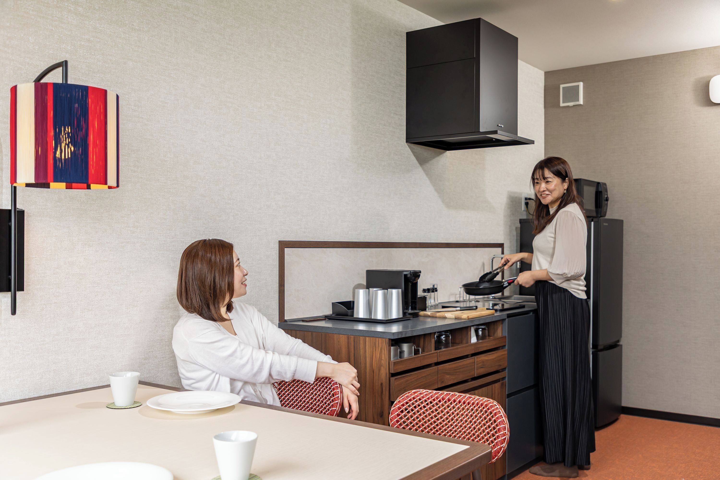 A compact kitchen with a dining area, a black range hood, and a coffee machine.
