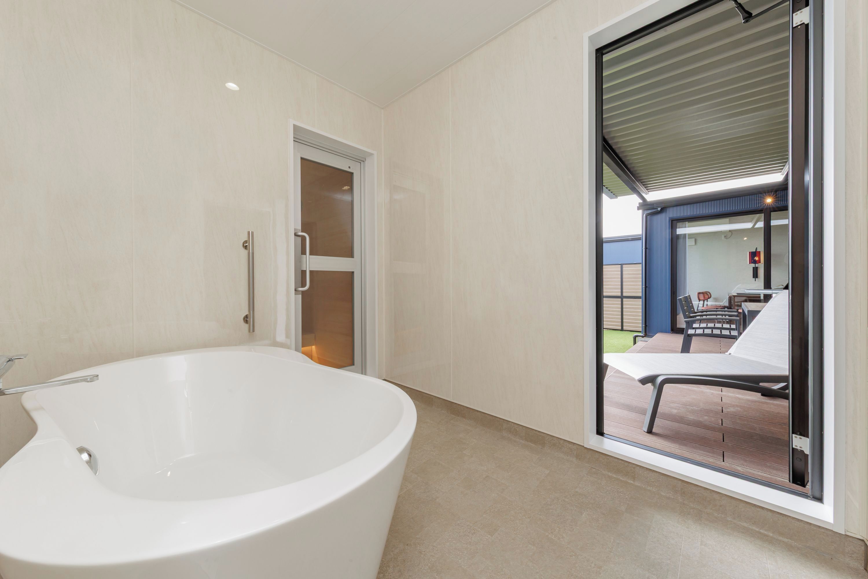 Un bagno moderno con una vasca freestanding, una porta vetrata che dà su un patio esterno con tavolo e sedie.