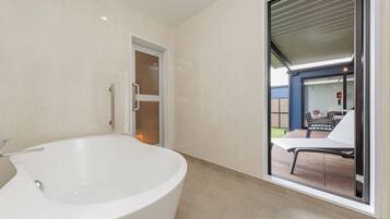 Un bagno moderno con una vasca freestanding, una porta vetrata che dà su un patio esterno con tavolo e sedie.