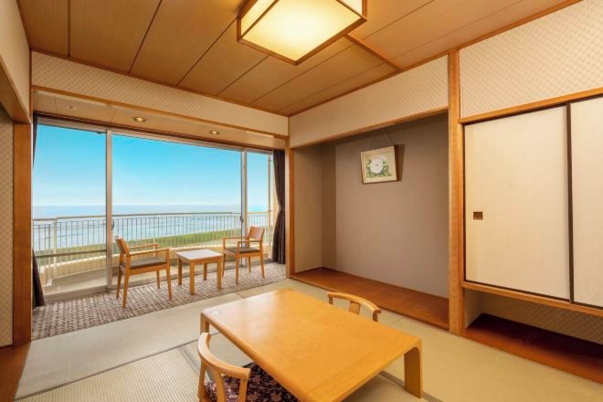 Una habitación japonesa tradicional con suelo de tatami, una mesa de madera y vistas al mar a través de amplios puertas correderas.