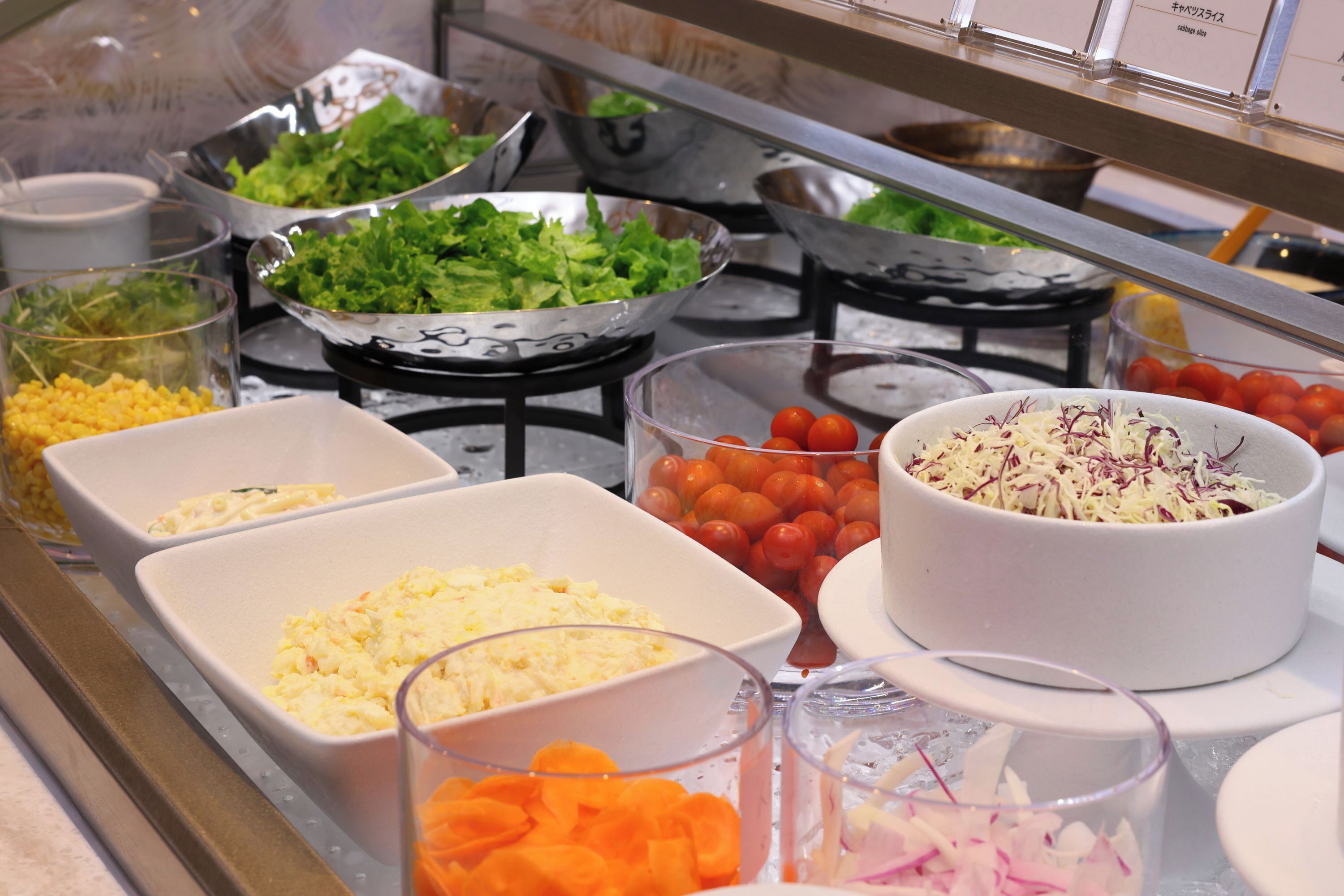Un bufé con diversos alimentos, como ensaladas, verduras y queso.