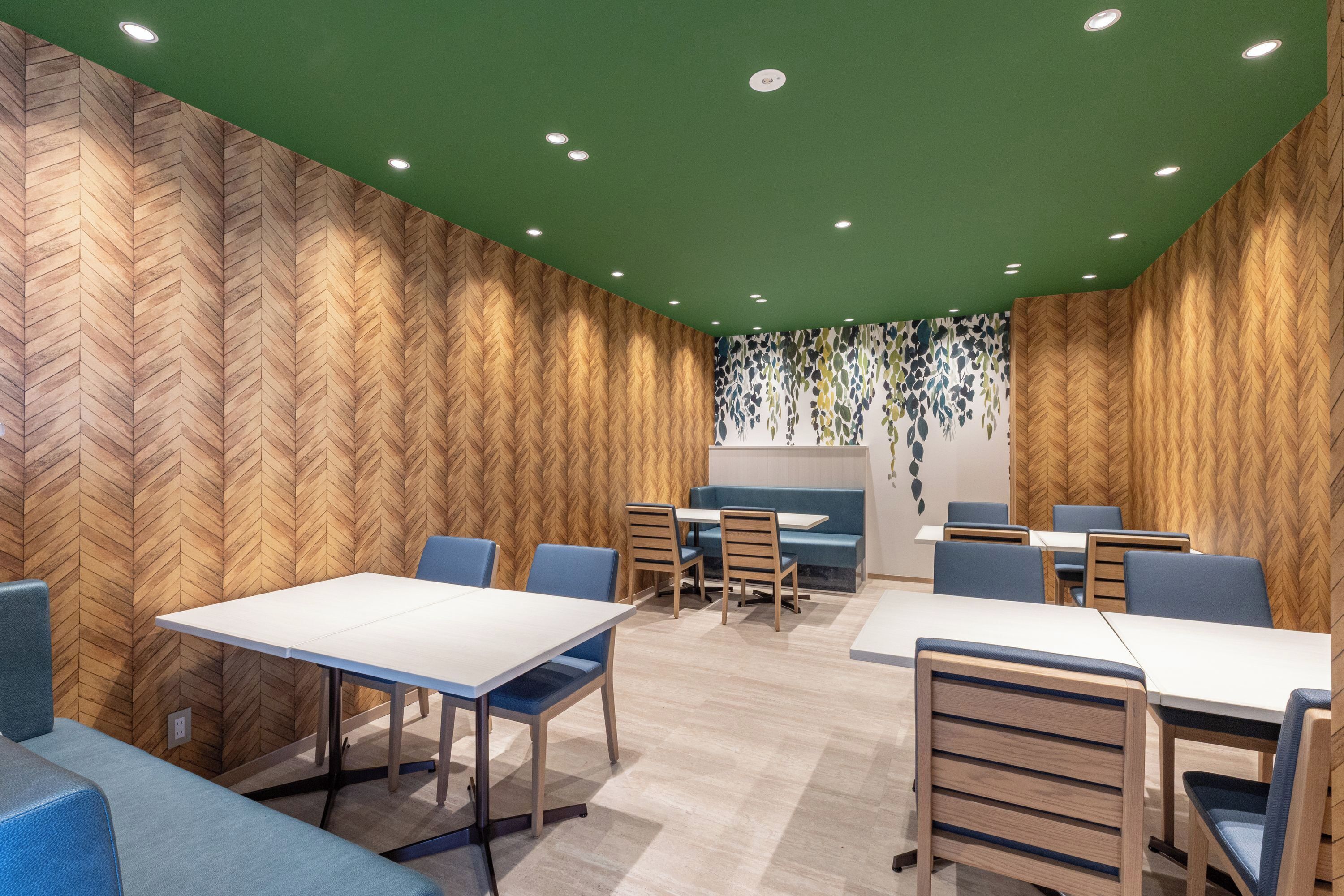 A modern dining area with wooden panel walls, green ceiling, and multiple seating arrangements including tables and booths.