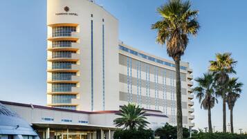 A modern hotel with a curved facade, multiple balconies, and palm trees in the foreground.