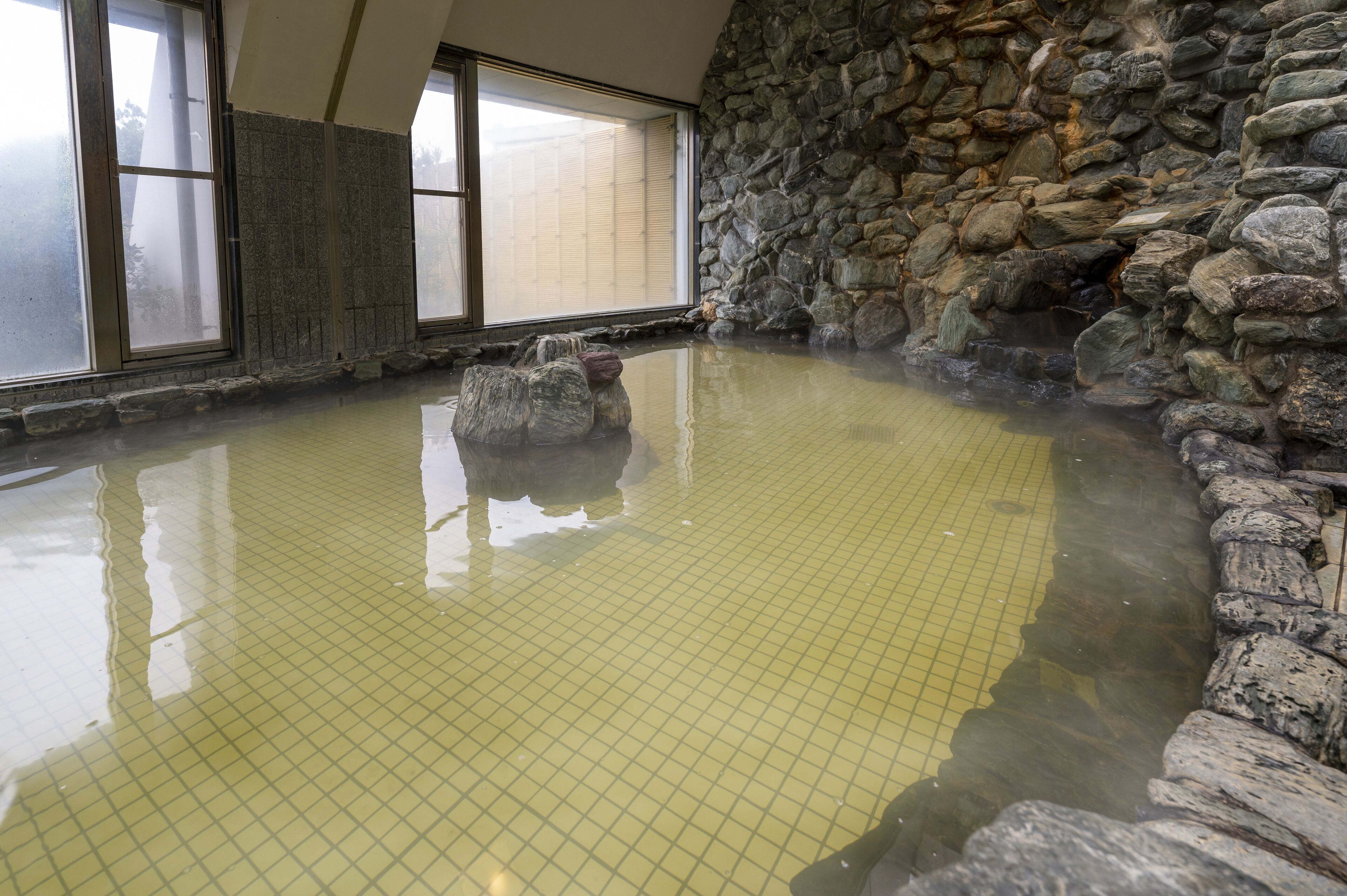 A hot spring bath with a stone wall and tiled floor.