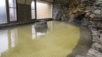 A hot spring bath with a stone wall and tiled floor.