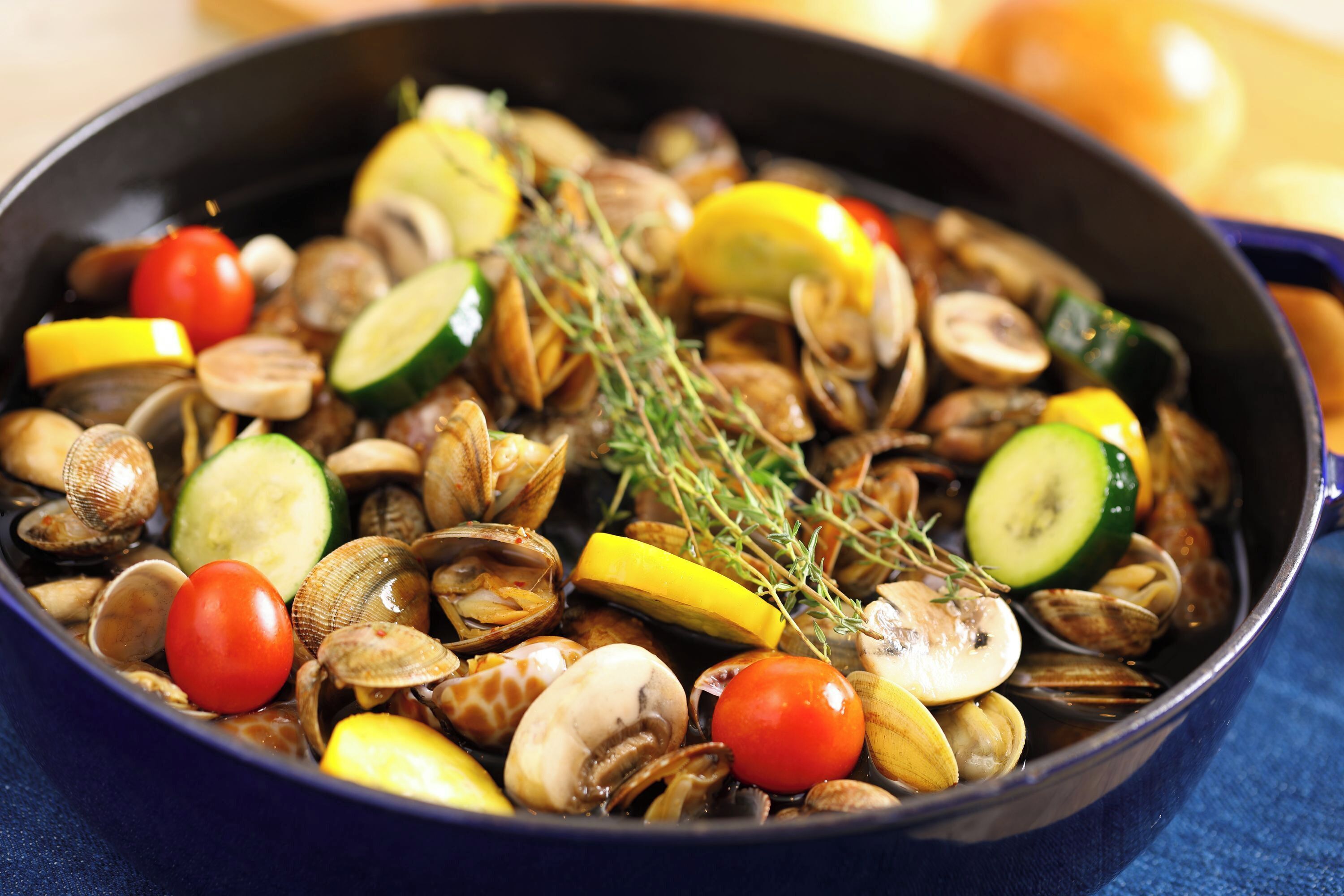 A pan filled with clams, cherry tomatoes, zucchini, and lemon slices.
