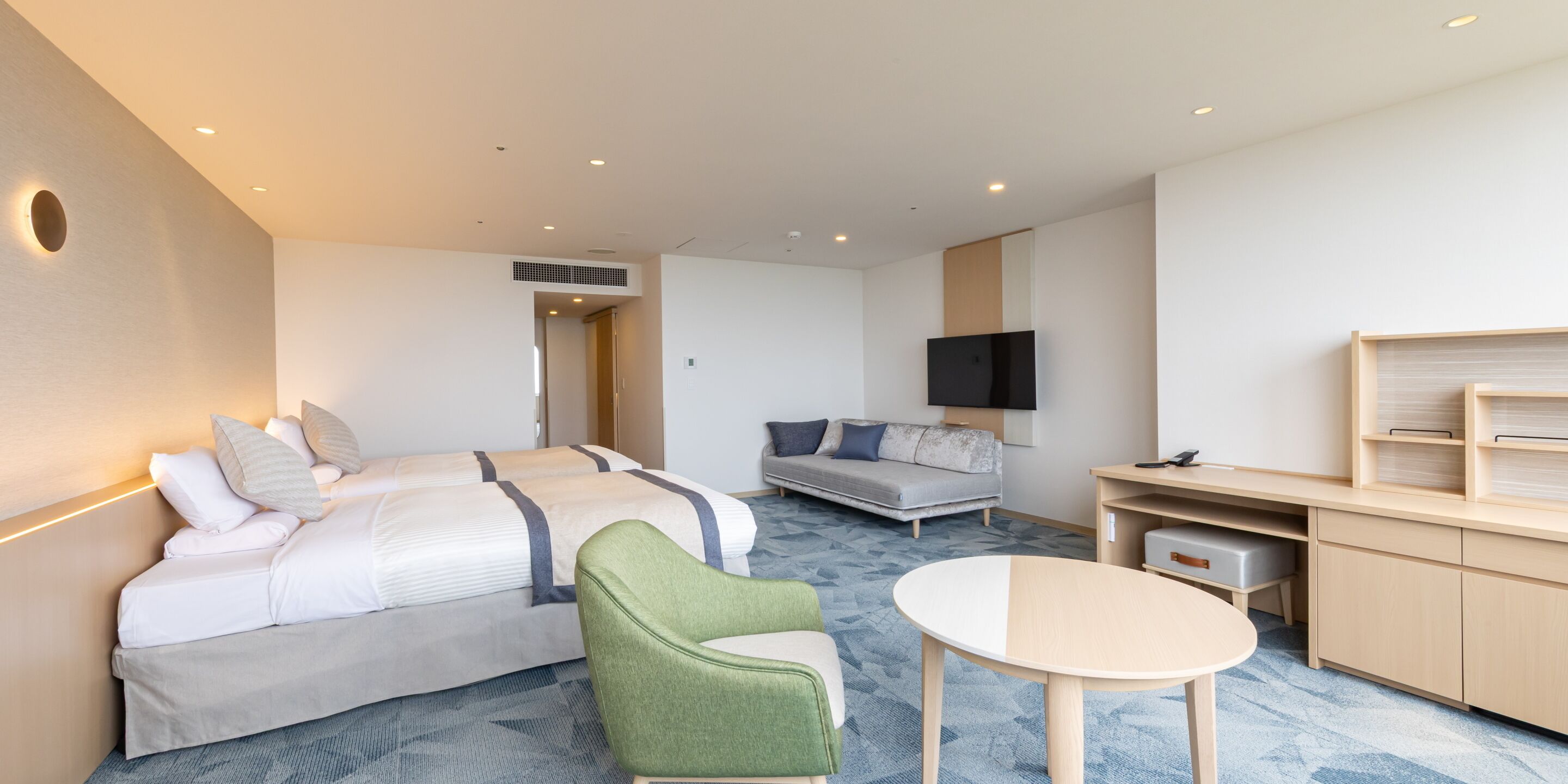 Une chambre d’hôtel moderne avec un lit, un canapé, un fauteuil vert et une petite table.