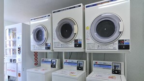Fila de lavadoras blancas con paneles de control, una máquina expendedora y un cartel con texto cirílico.