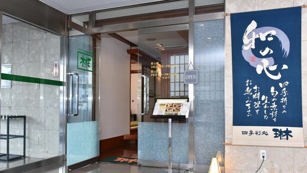 L’entrée d’un hôtel, avec une porte en verre, un comptoir d’accueil et une affiche ornée de caractères japonais.