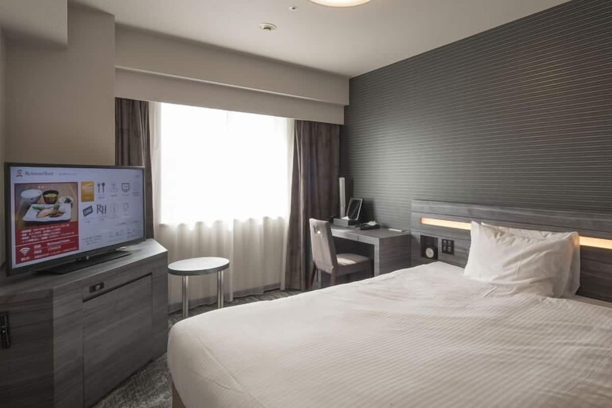 A hotel room with a bed, a desk, a chair, a television, and a window with curtains.