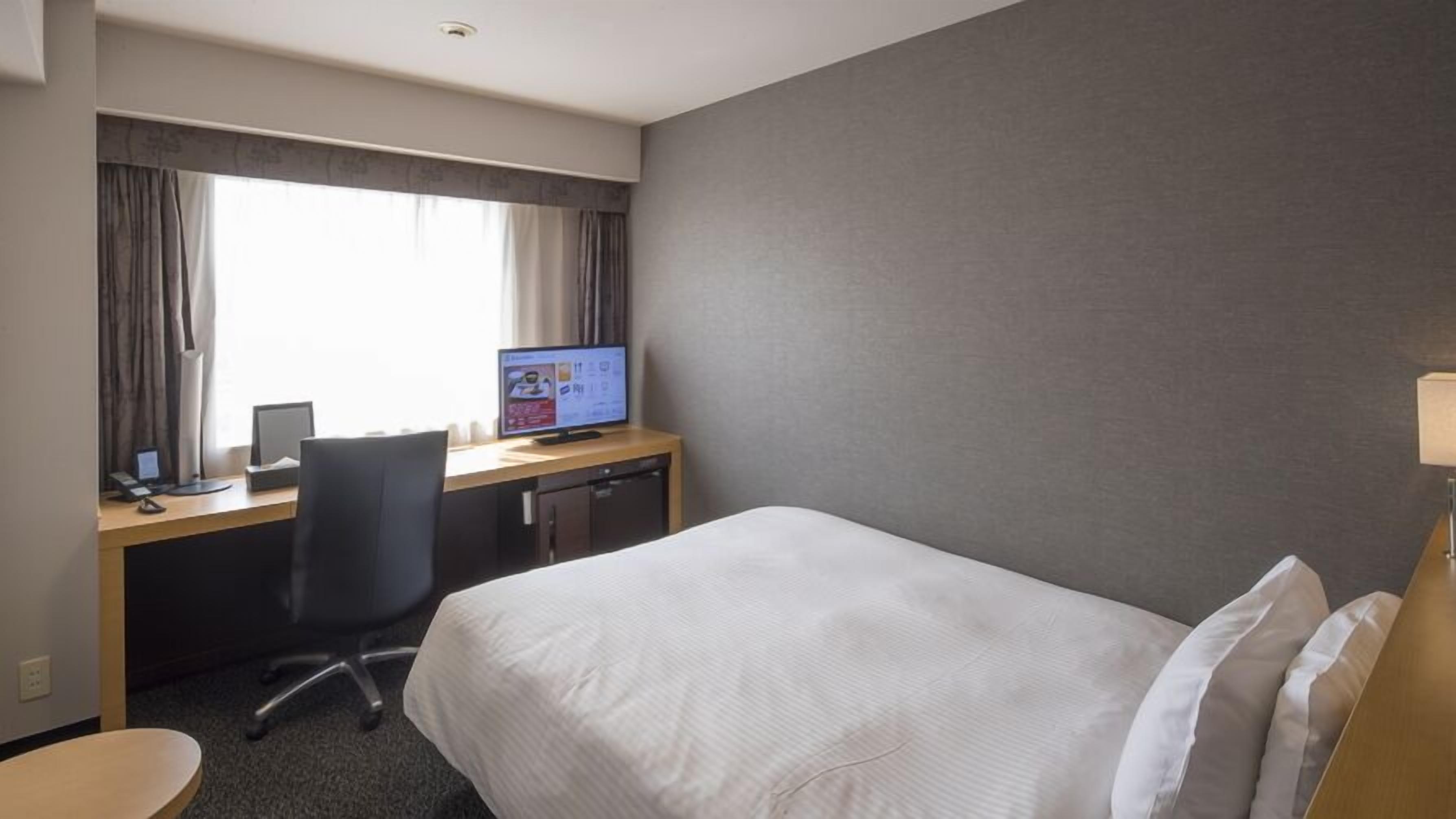 Una habitación de hotel con una cama, un escritorio con computadora, una silla y una ventana con cortinas.