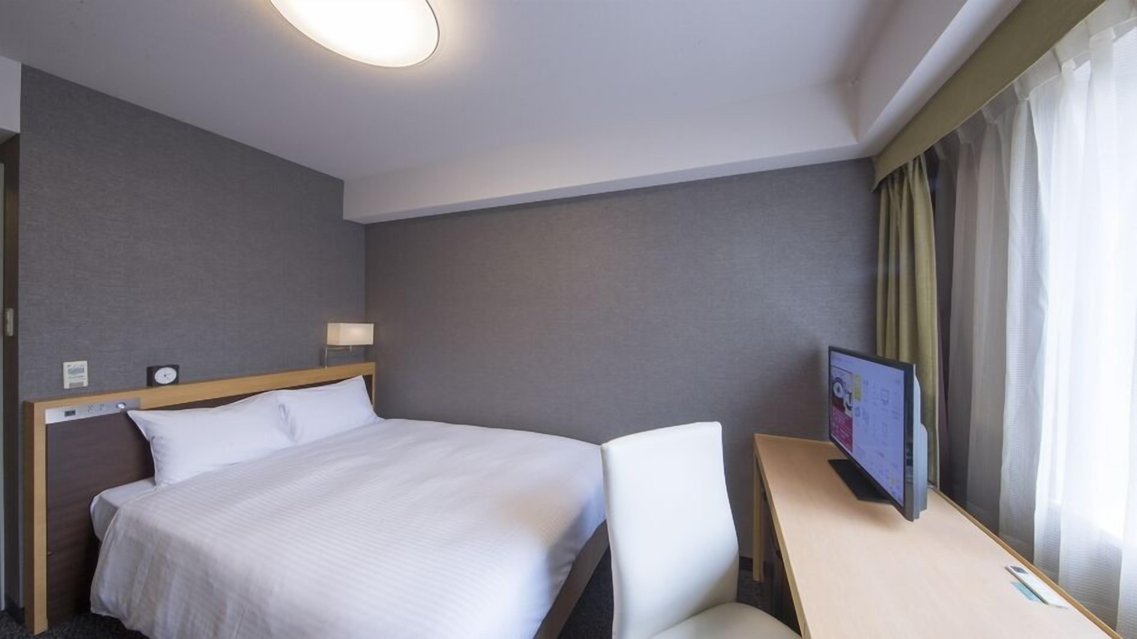 Una habitación de hotel con cama, escritorio, televisor y ventana con cortinas.