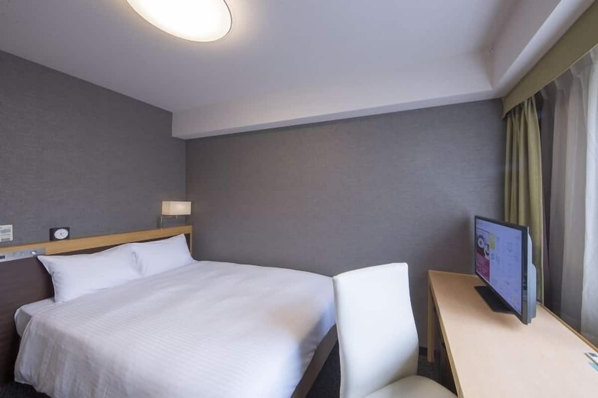 A hotel room with a bed, a desk, a TV, and a window with curtains.
