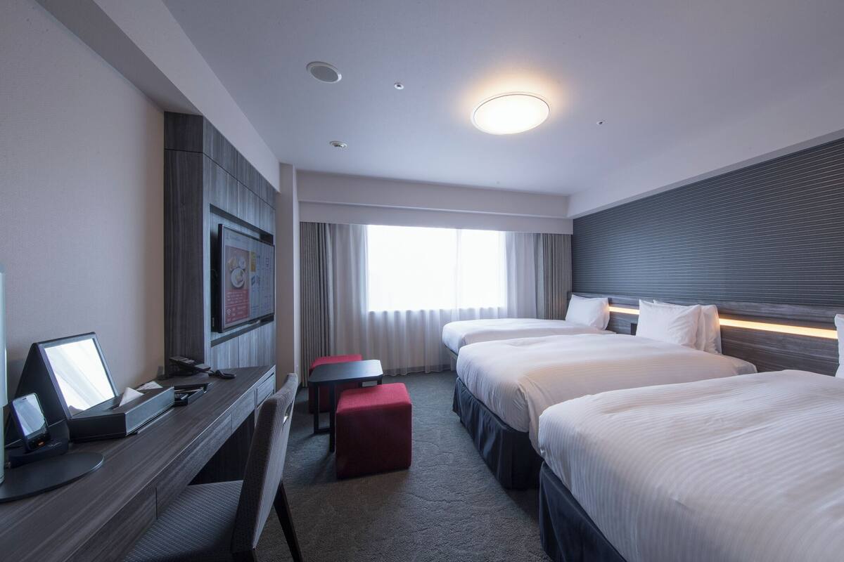 A hotel room with a desk, two beds, a TV, and a window with curtains.