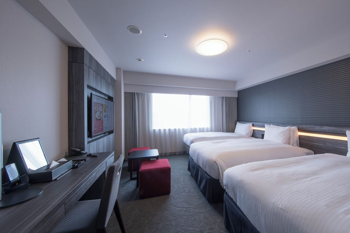 Una habitación de hotel con escritorio, dos camas, televisión y ventana con cortinas.