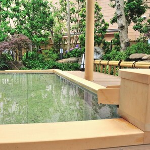 Une piscine rectangulaire entourée d’une terrasse en bois, située dans un espace paysager agrémenté de diverses plantes et arbres.