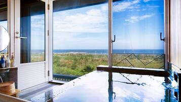 A room with a large window overlooking a landscape, a bathtub, and a wooden bench.