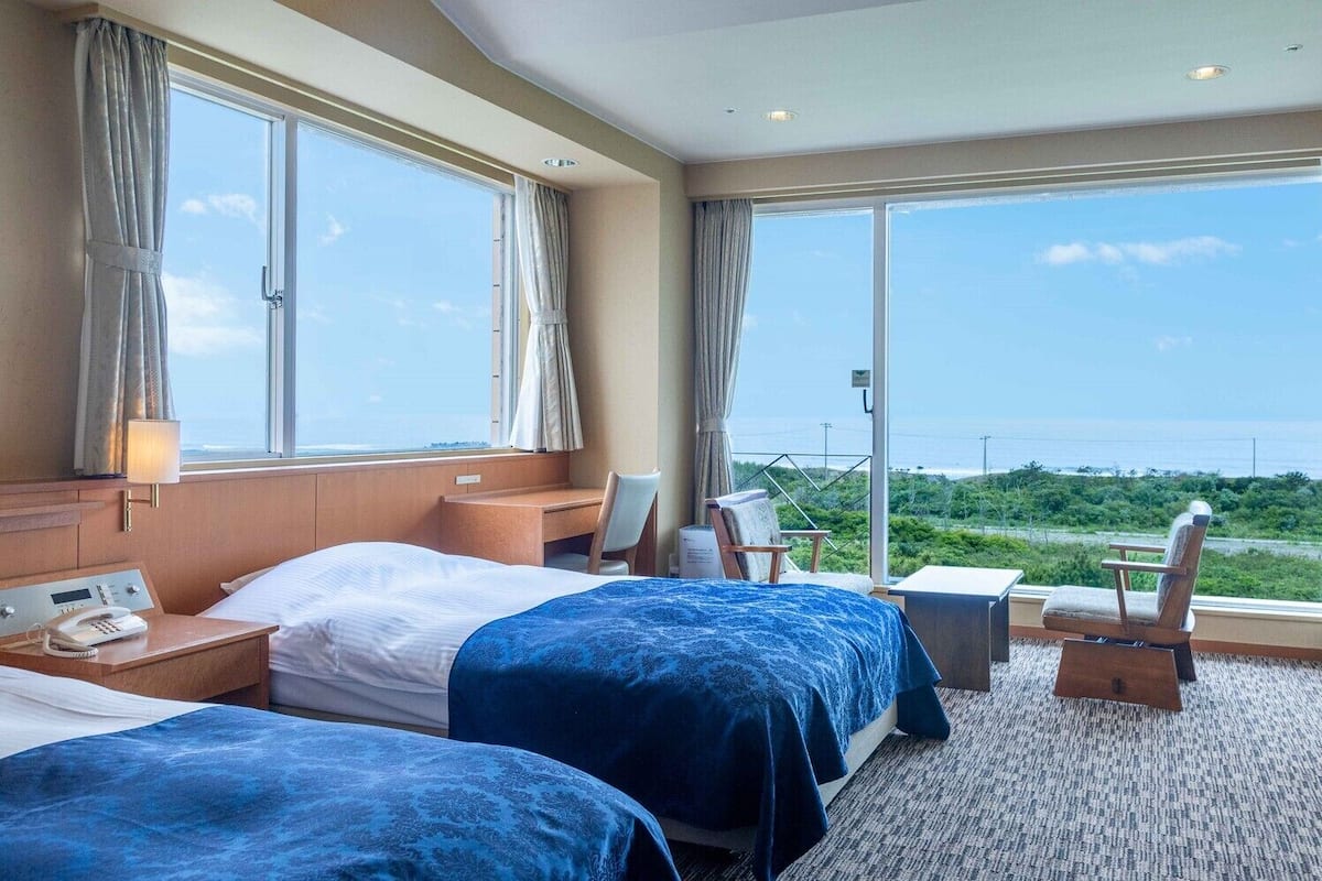 Une chambre d’hôtel avec deux lits, un bureau, une chaise et une vue sur l’océan.