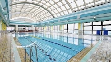 An indoor swimming pool with a high ceiling and large windows.