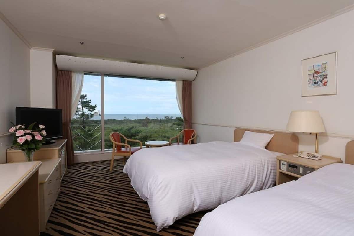 Une chambre d’hôtel avec deux lits, un bureau, une chaise, une télévision, une lampe et une fenêtre donnant sur un beau paysage.