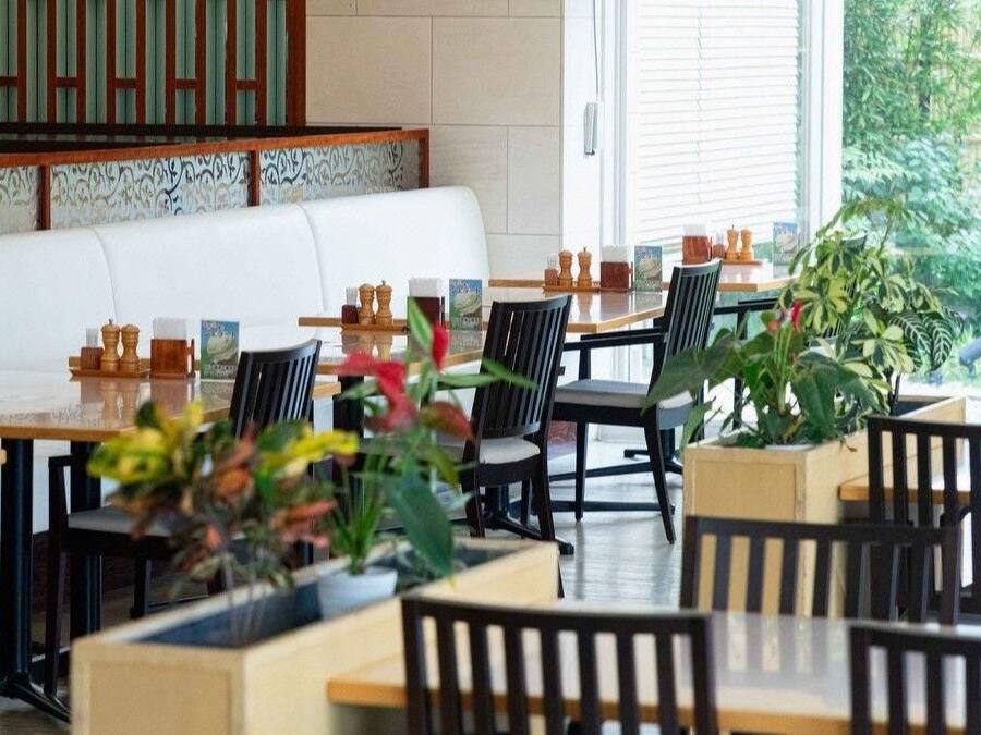 A restaurant with multiple tables and chairs, a white cushioned bench, and potted plants.