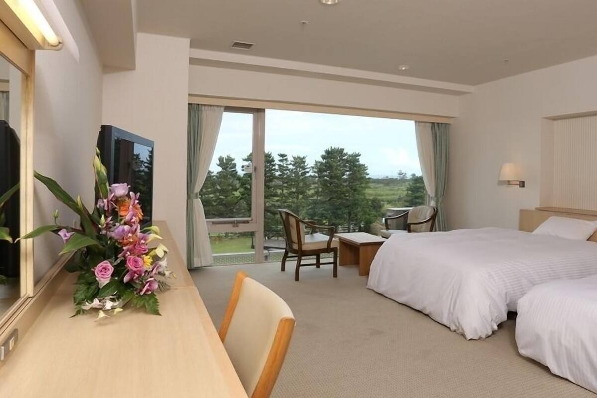 Une chambre d’hôtel comprenant un lit, un bureau, une chaise, une télévision et un balcon avec vue sur les arbres.