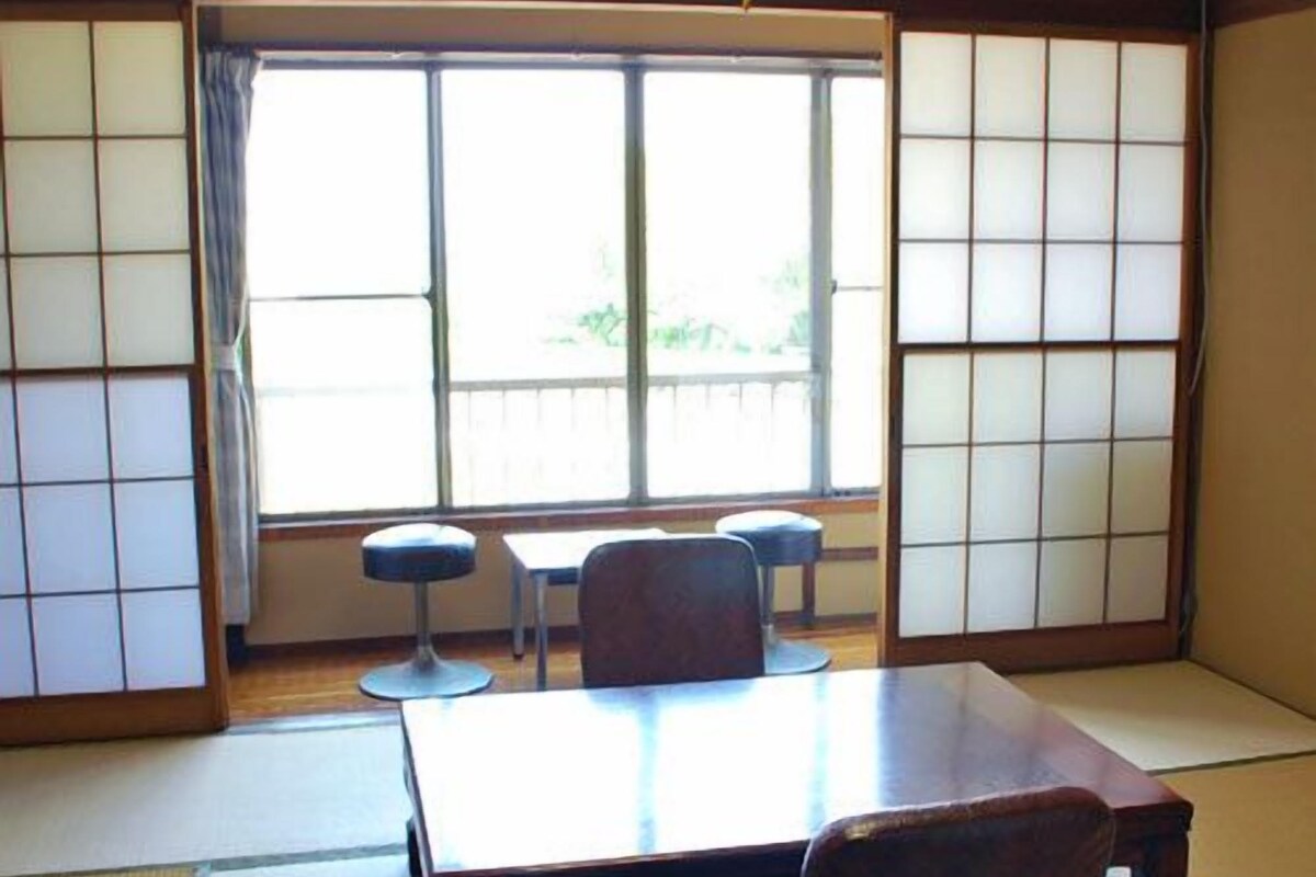 A traditional Japanese room with tatami flooring, a low table, two chairs, and sliding shoji doors.