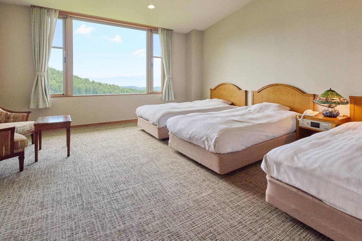 Ein Hotelzimmer mit zwei Betten, einem Schreibtisch, einer Lampe und Blick ins Freie.