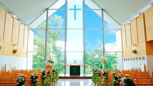 Interior de igreja com bancos de madeira, altar central com cruz e janelas amplas.