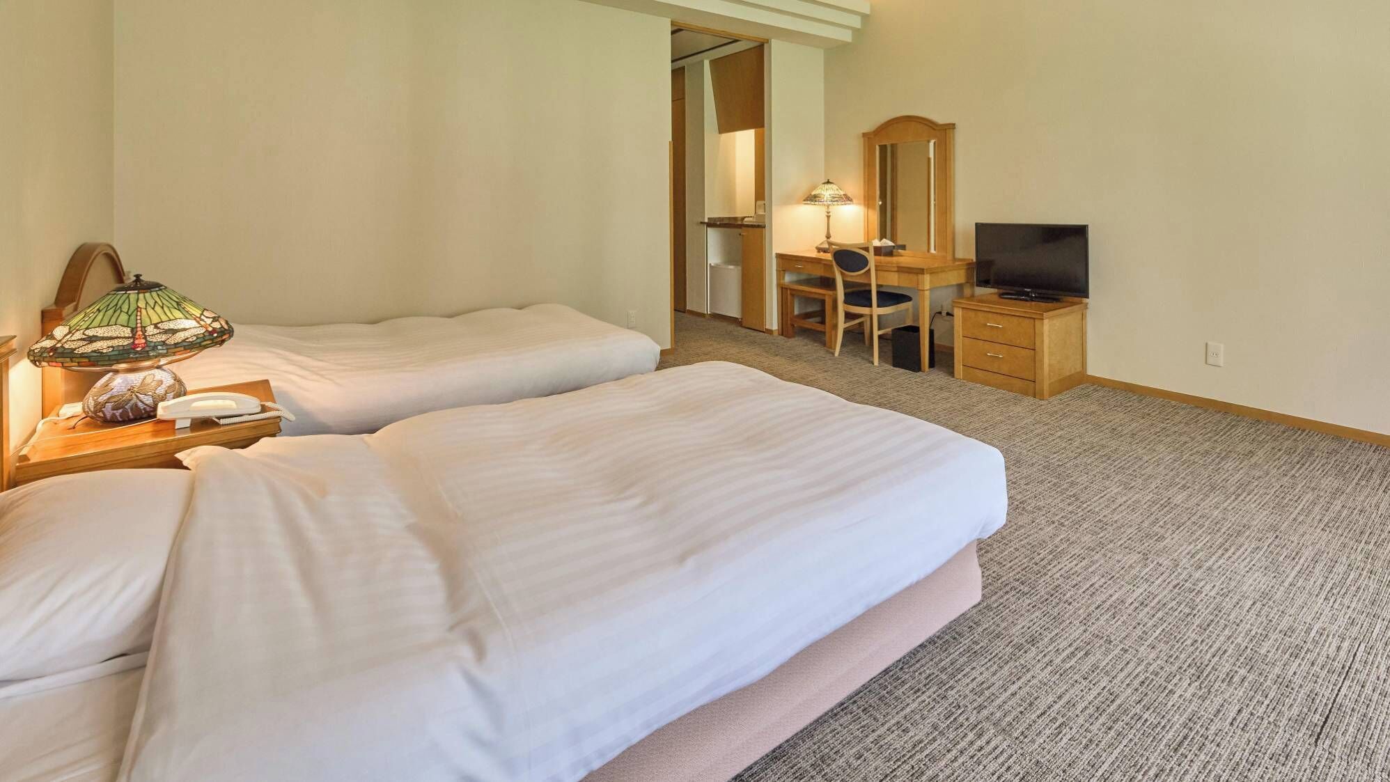 A hotel room with two beds, a desk with a chair, a television, and a lamp.