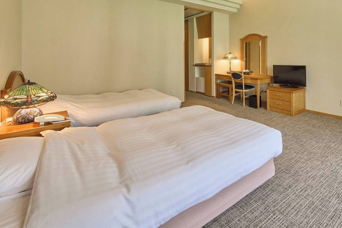 Ein Hotelzimmer mit zwei Betten, einem Schreibtisch mit Stuhl, einem Fernseher und einer Lampe.