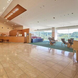 Un lobby espacioso con una recepción, una zona de estar con sillas y grandes ventanales con vistas al exterior.
