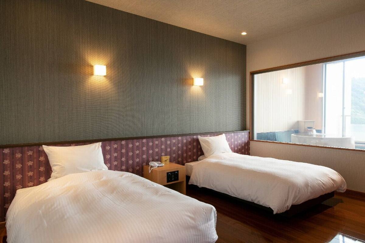 A hotel room with two beds, a large window, and a view of the outside.