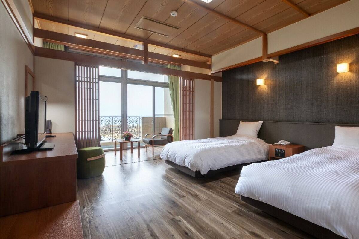 A hotel room with two beds, a desk with a television, and a balcony with a view.