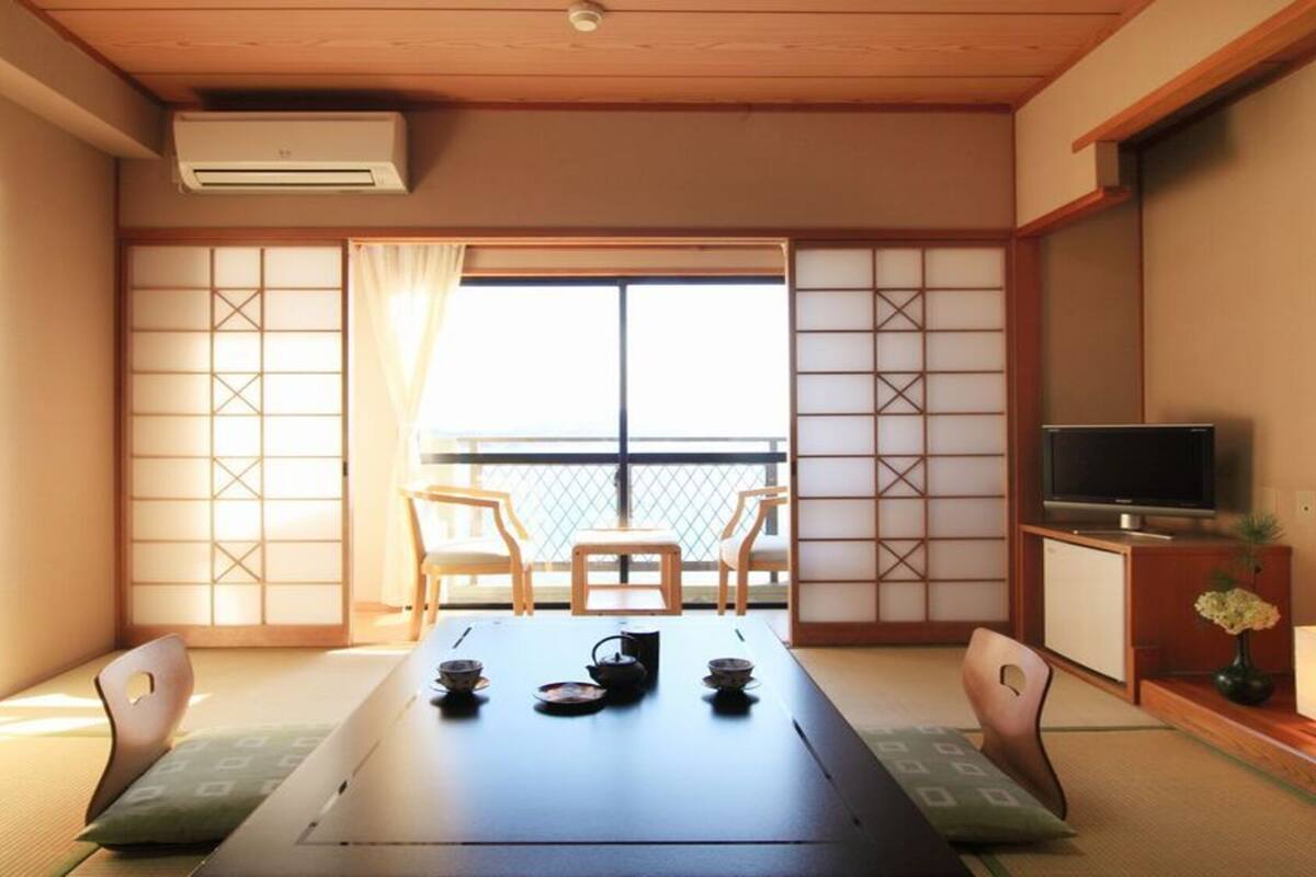 A traditional Japanese room with tatami flooring, a low table with tea set, sliding doors, and a TV on a wooden stand.