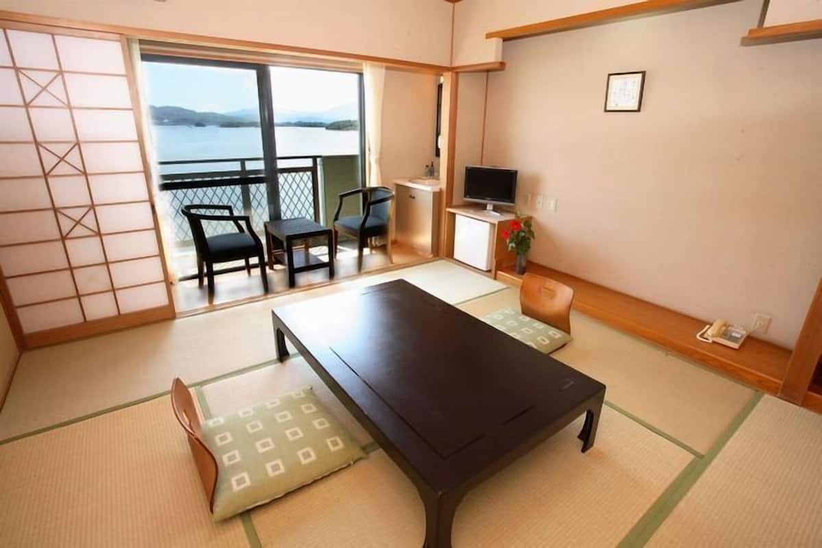 A room with tatami flooring, a low table, chairs, a TV, and a view of the water.