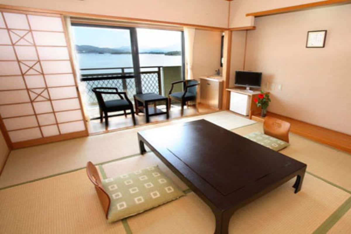 A traditional Japanese room with tatami flooring, a low table, a sofa, and a sliding door leading to a balcony with a view.