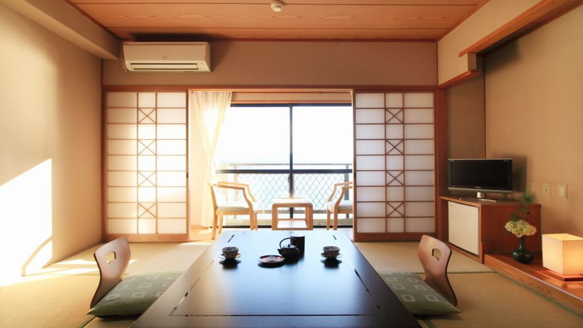 A traditional Japanese room with tatami flooring, a low table with tea set, sliding doors, and a TV on a wooden stand.