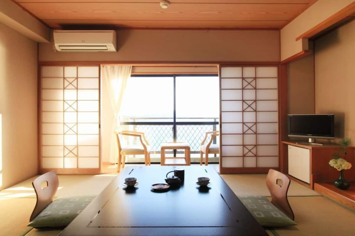 A traditional Japanese room with tatami flooring, a low table with tea set, sliding doors, and a TV on a wooden stand.