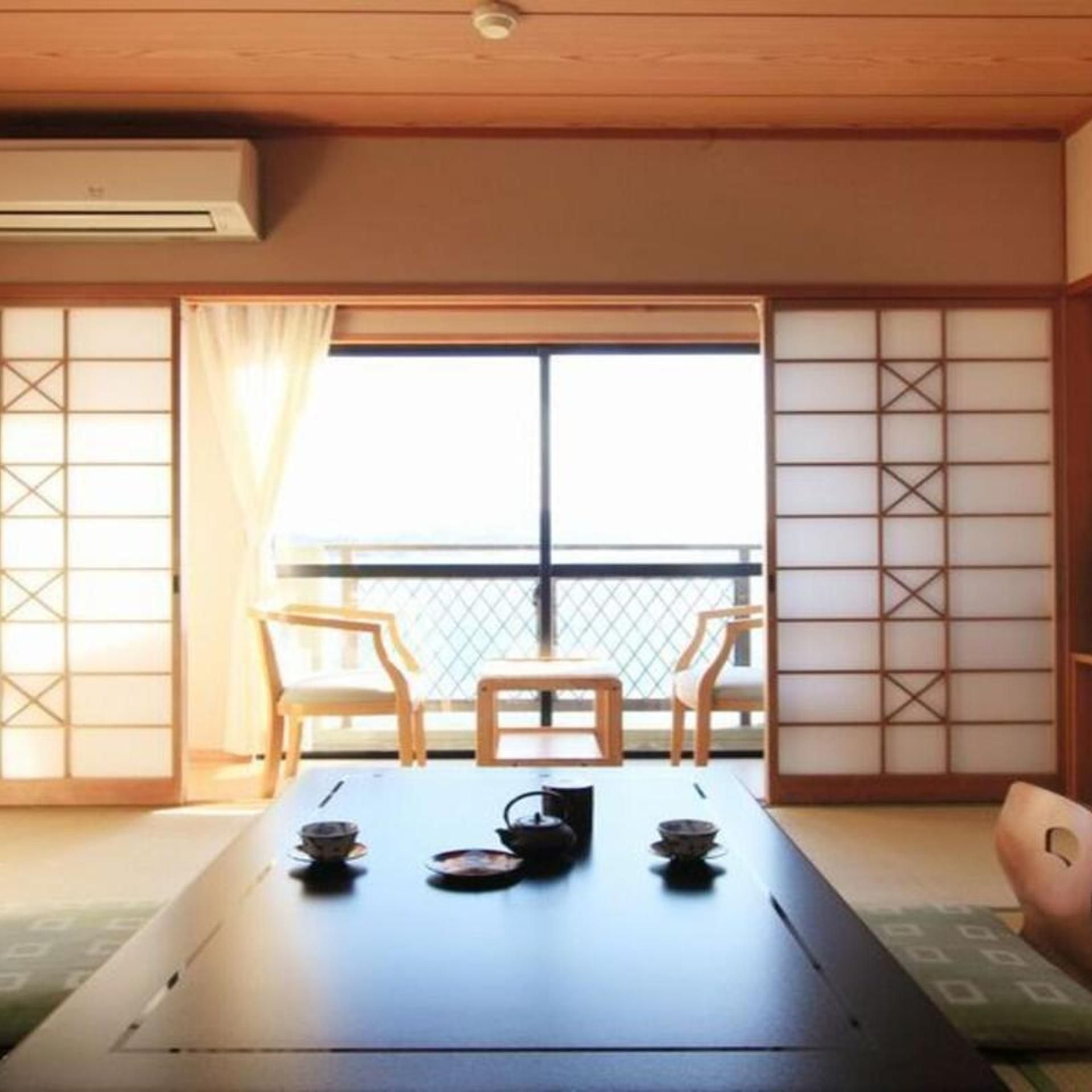 A traditional Japanese room with tatami flooring, a sliding door, and a view through a large window.