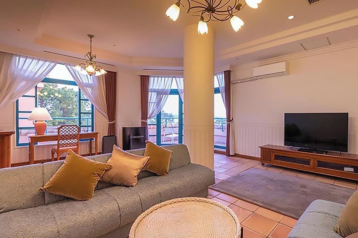 Ein Wohnzimmer mit einer Couch, einem Fernseher und Blick durch große Fenster.