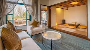 A modern hotel room with a sofa, a round woven coffee table, and a traditional tatami mat area. - Ooedo Onsen Monogatari Premium Saikaibashi (Sasebo)