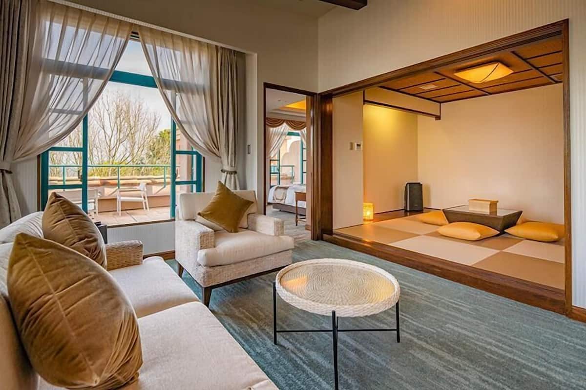 Ein modernes Hotelzimmer mit einer Couch, einem runden gewebten Couchtisch und einem Bereich mit traditionellen Tatami-Matten.