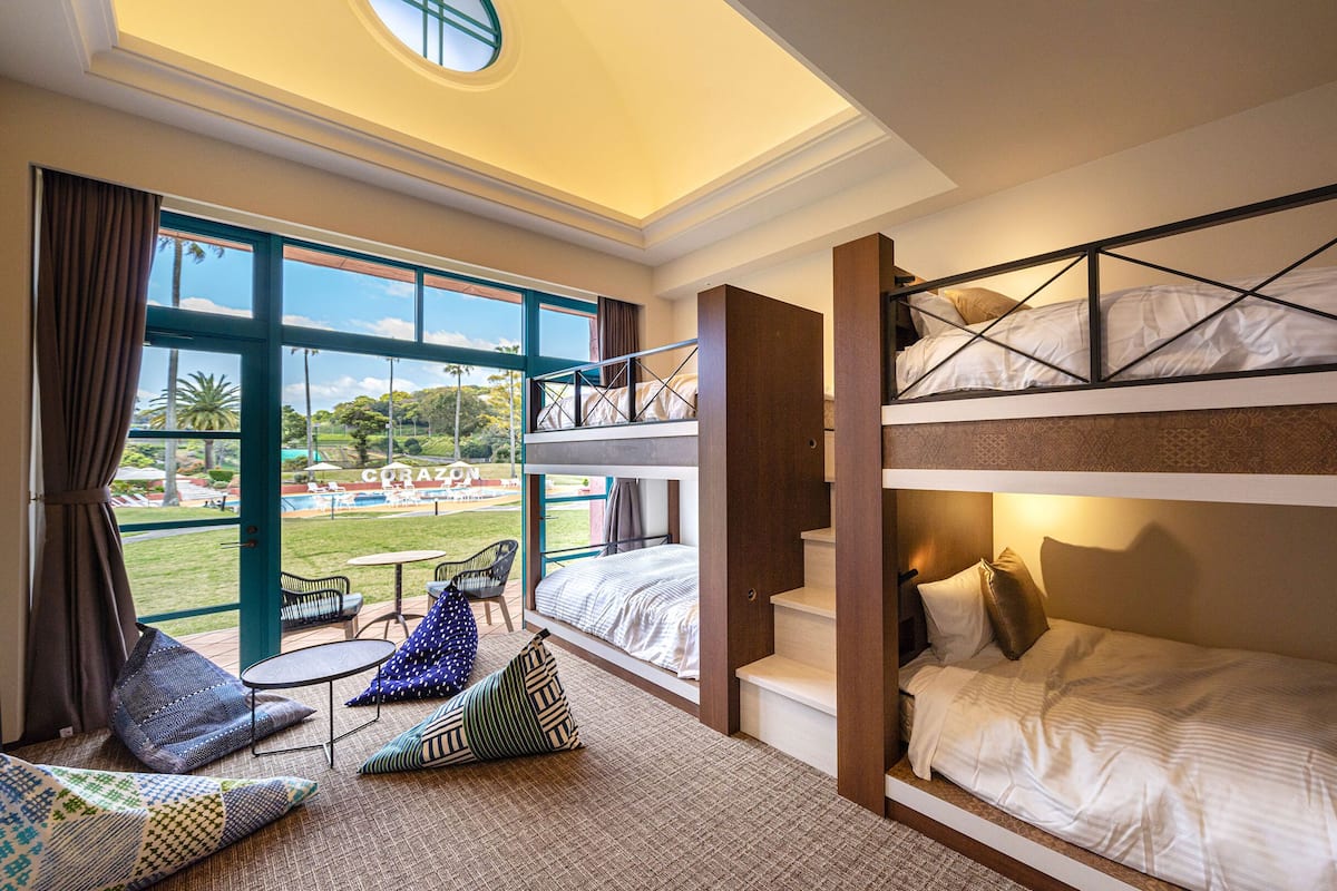 Ein Hotelzimmer mit Blick auf einen Pool und einen Tennisplatz, mit Stockbetten, einem kleinen Tisch und zwei Stühlen.