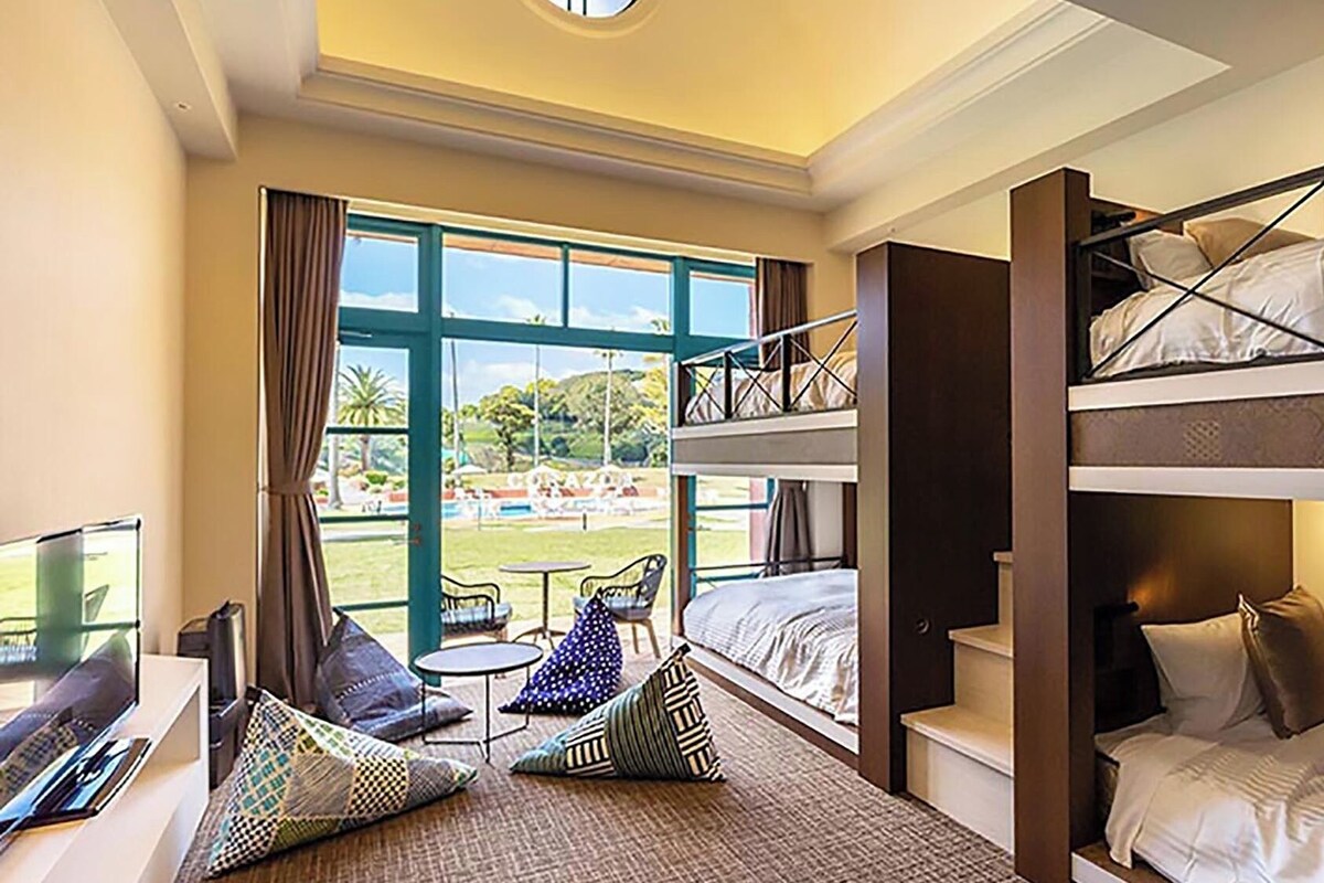 Ein Hotelzimmer mit Etagenbetten, einem Fernseher, einem kleinen Tisch und Blick auf einen Pool und Grünflächen.