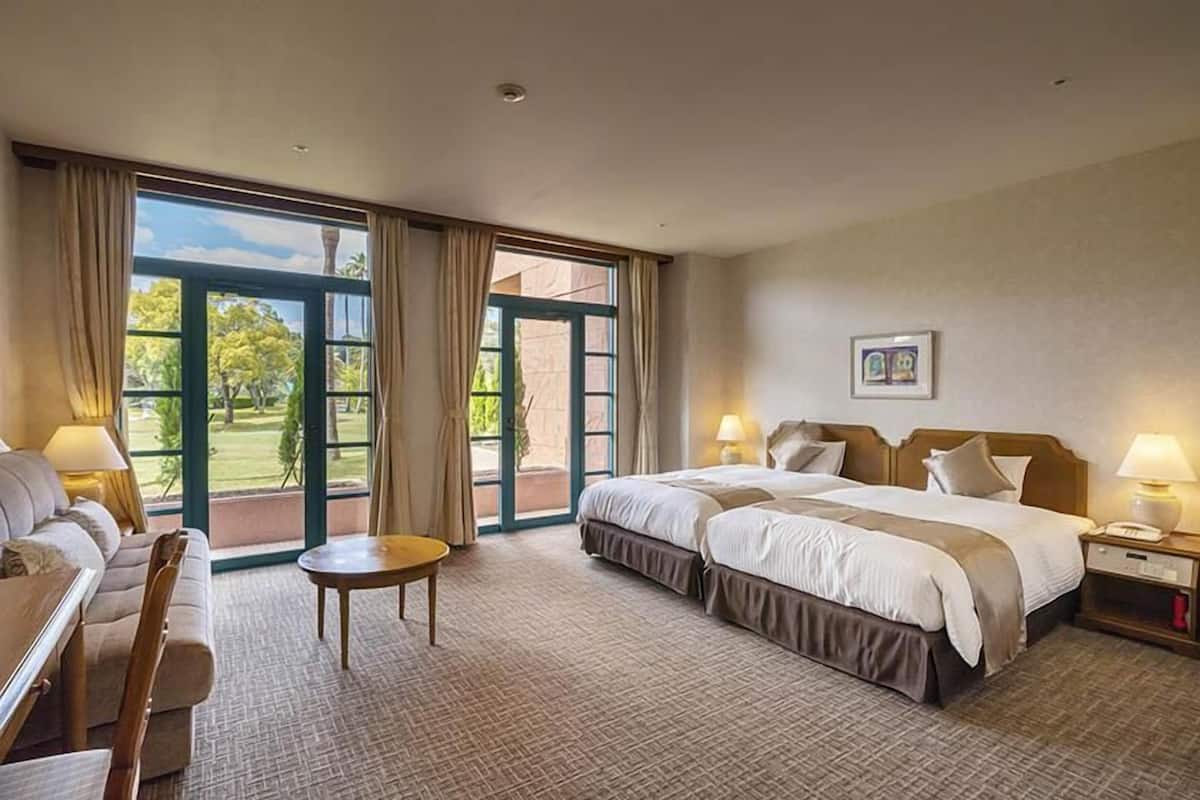 Ein Hotelzimmer mit einem großen Bett, einer Couch, einem kleinen Tisch und Blick ins Freie durch große Fenster.