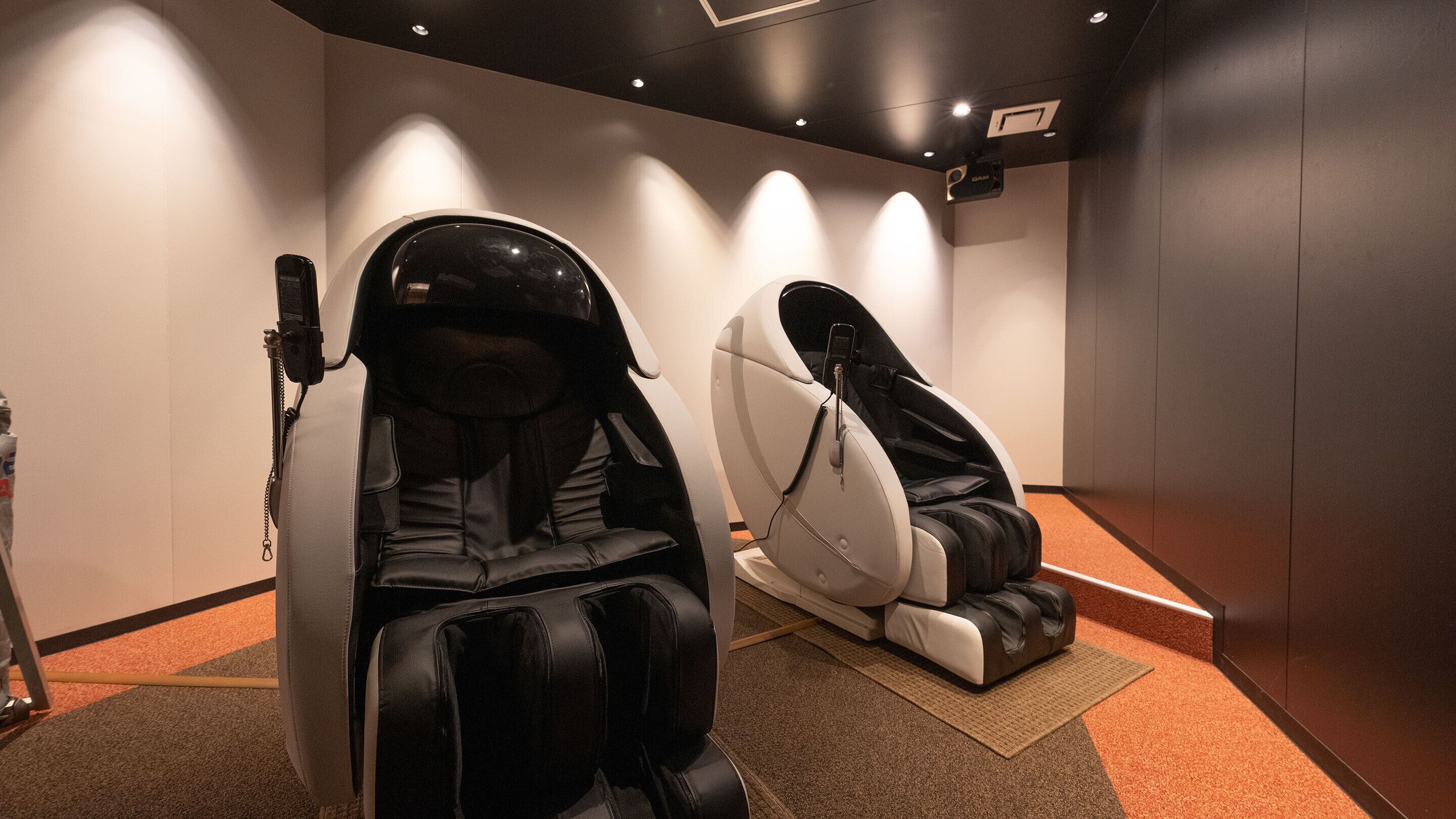 Two massage chairs in a room with a carpeted floor and a ceiling with recessed lighting.