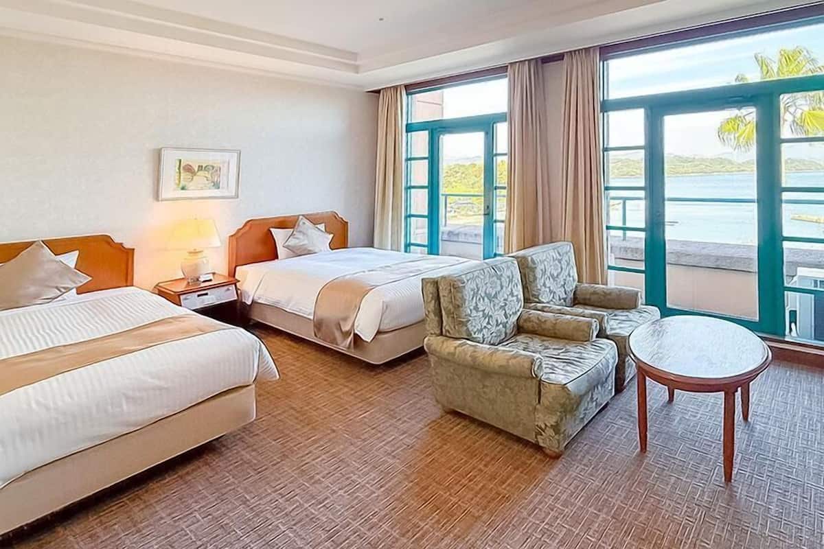 Ein Hotelzimmer mit zwei Betten, einem Sofa, einem kleinen Tisch und einem großen Fenster mit Blick auf das Wasser.