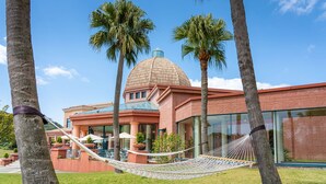 A building with a dome and a red facade, surrounded by palm trees and a hammock. - Ooedo Onsen Monogatari Premium Saikaibashi (Sasebo)